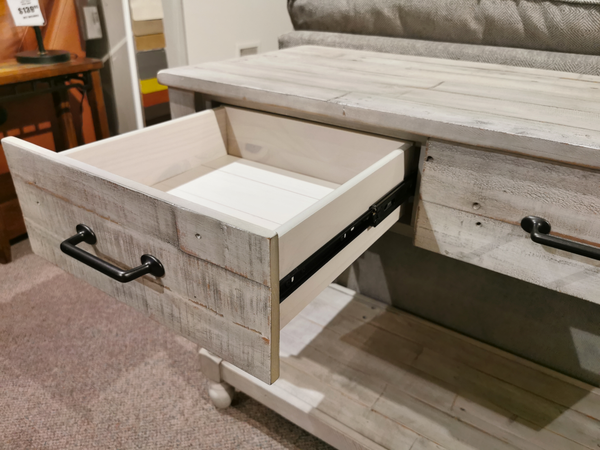 A solid pine wood drawer with a black handle is partially open in the Ashley Shawnalore Sofa Table.