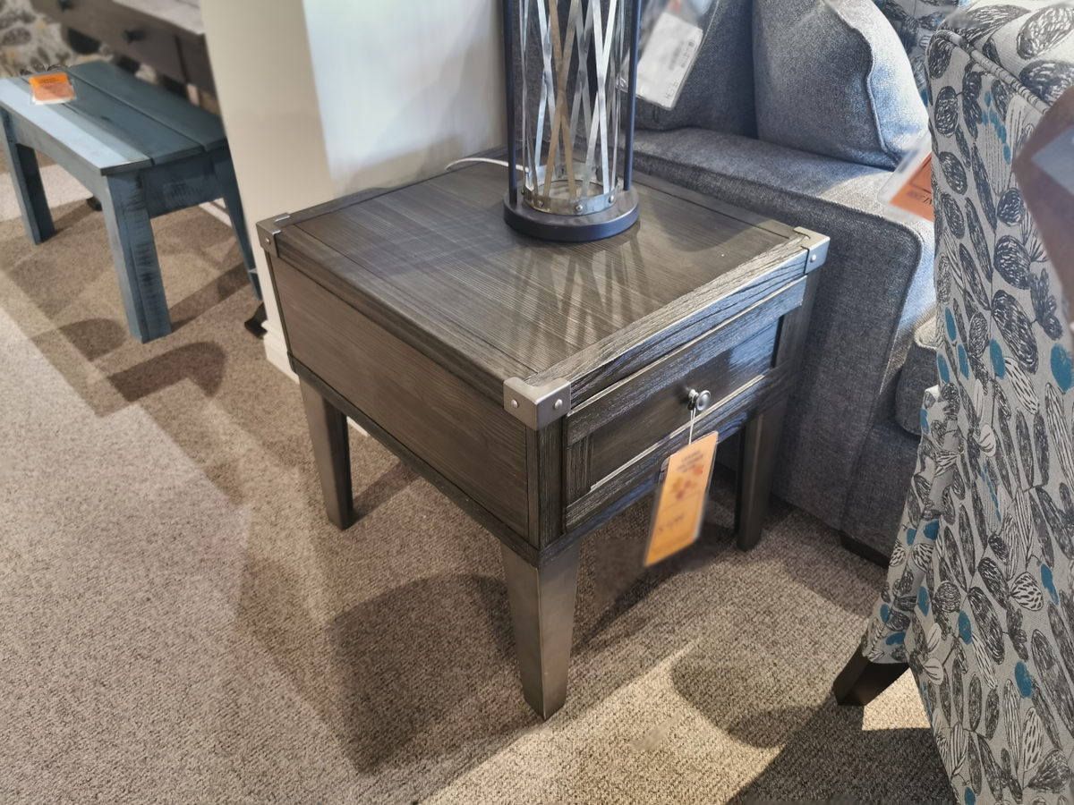 The Tadoe End Table by Ashley is perfect for a rustic-industrial setting with its drawer and lamp by the sofa.
