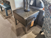 The Tadoe End Table by Ashley is perfect for a rustic-industrial setting with its drawer and lamp by the sofa.