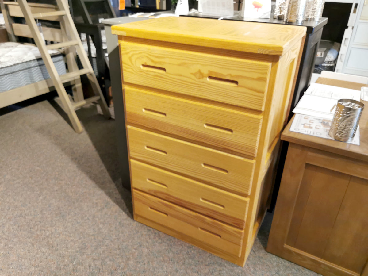 The Crate A7015 5 Drawer Chest with dovetailed corners stands by a desk and bunk bed in a furniture store.