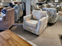 The 2570 Stationary Chair by Decor-rest, with its modern pattern, is displayed in a furniture store. It is surrounded by various other chairs and tables on a carpeted floor, making it an excellent choice for compact living areas.