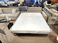 A 2T3 Queen Transformer Sofa Bed from Decor-rest, with the mattress extended and covered in plastic, is prominently displayed in a furniture store showroom.