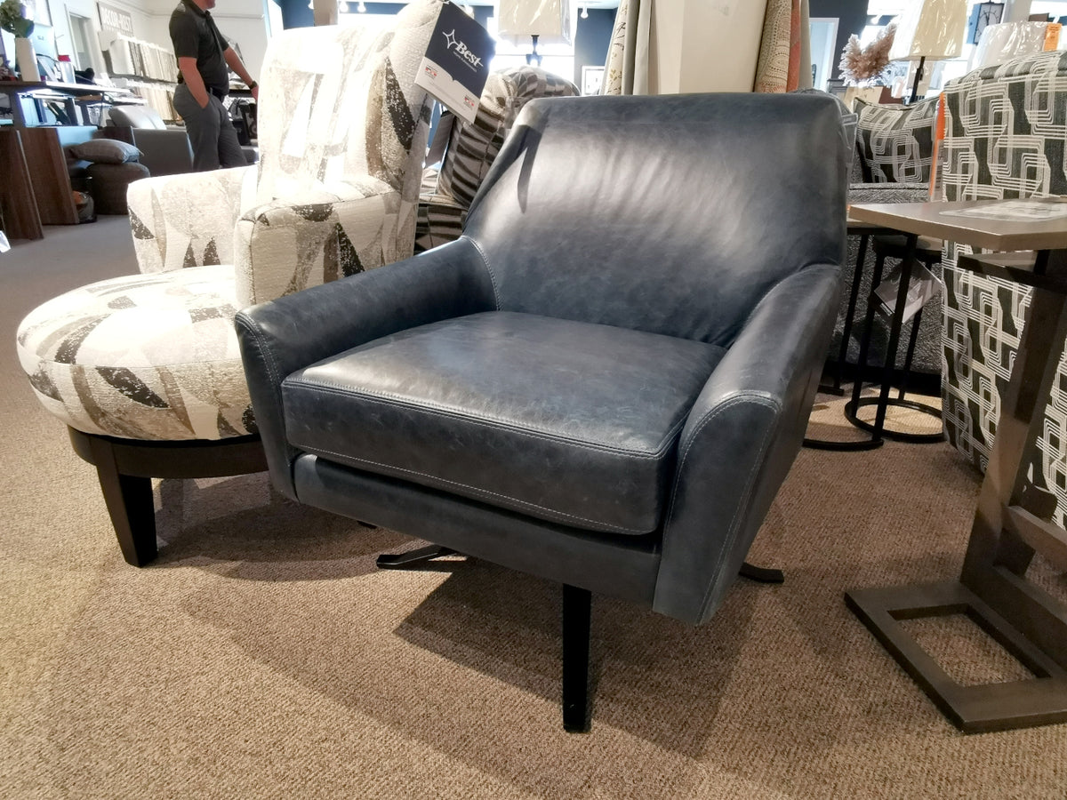 The Decor-rest 3097 Leather Swivel Chair, featuring a contoured back in a striking blue leather finish, is elegantly showcased in a furniture store. Amidst an array of chairs and tables and set on a carpeted floor, this piece embodies the essence of mid-century modern design.