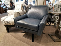 The Decor-rest 3097 Leather Swivel Chair, featuring a contoured back in a striking blue leather finish, is elegantly showcased in a furniture store. Amidst an array of chairs and tables and set on a carpeted floor, this piece embodies the essence of mid-century modern design.