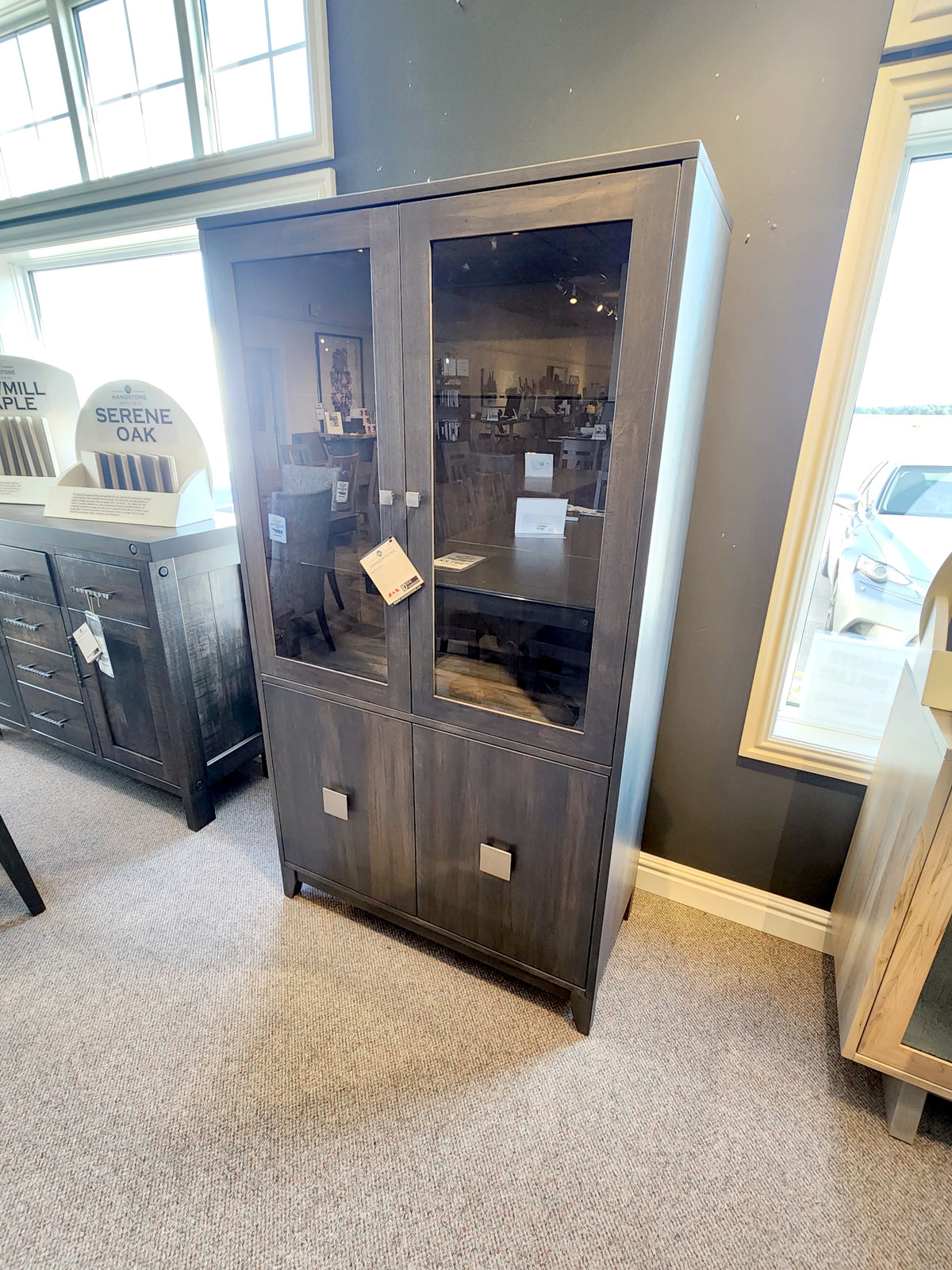 The BE270 Belmont Display Cabinet by Handstone, with glass doors, shines in showrooms with its solid dark wood design.