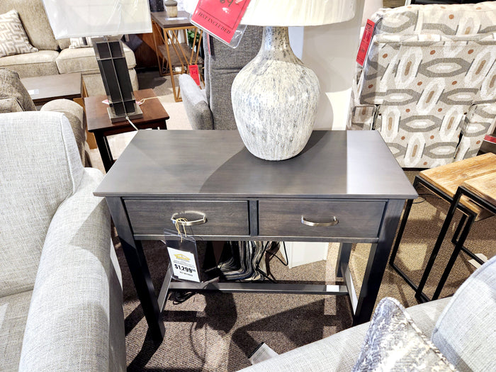 The Handstone BR125 Brooklyn Sofa Table features a contemporary style with dark wood, silver handles, and a gray lamp.