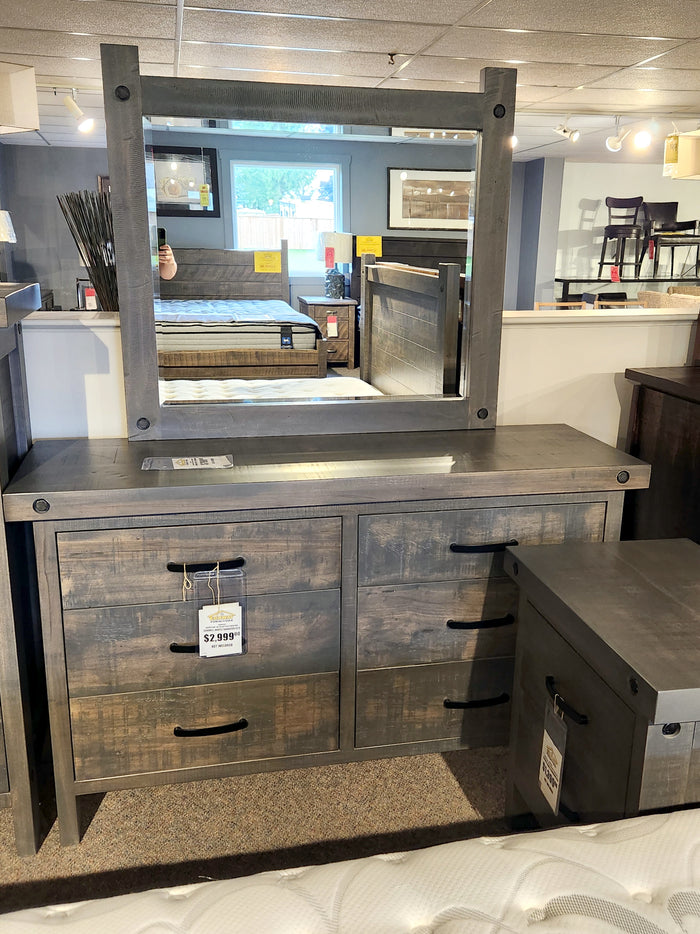 The Handstone Rafters Six Drawer Dresser with mirror is displayed in a furniture showroom.