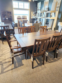 The Handstone RA4284 Rafters Dining Package features a wooden table and eight rustic chairs, displayed in a showroom.