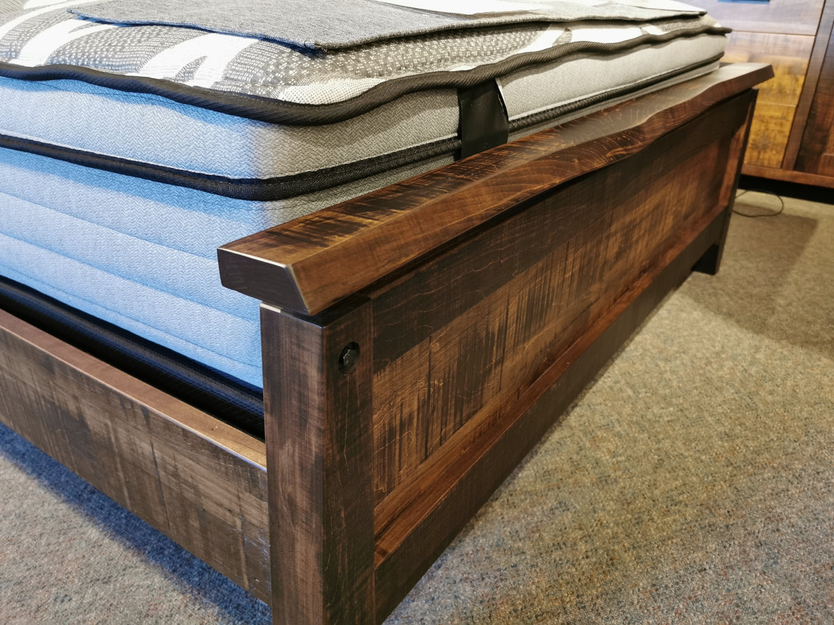 Close-up of a Handstone PE-QL Pemberton Q Bed with sculpted curves, blue mattress, and blanket on carpeted floor.