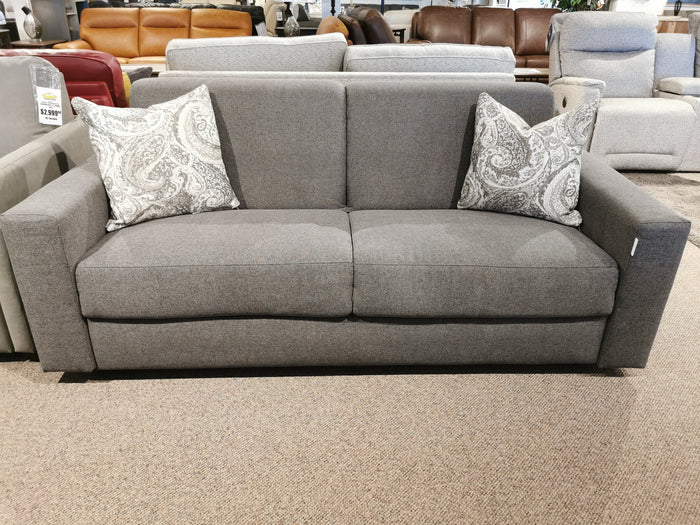 Primo Giotto Double Sofa Bed in gray, shown with two patterned throw pillows in a furniture showroom.