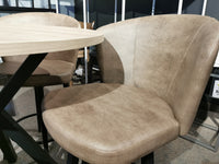 A beige upholstered chair with texture sits by a 39" Amisco laminate round table in a carpeted room.