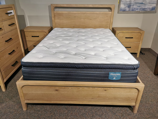 The Magnussen B5684 Somerset Queen Bed Frame with mattress is between two nightstands in a carpeted room.