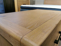 Close-up of a Magnussen B5684 Somerset Nightstand with USB charger, smooth top, next to a bed and bedroom furniture.