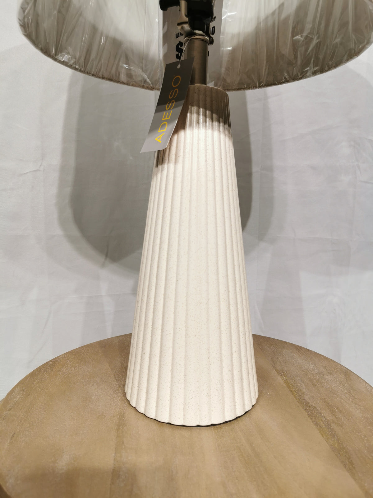A cream pleated Lana 2 Pack Table Lamp by Adesso Lamp with oatmeal linen shade sits on a round light wood surface.
