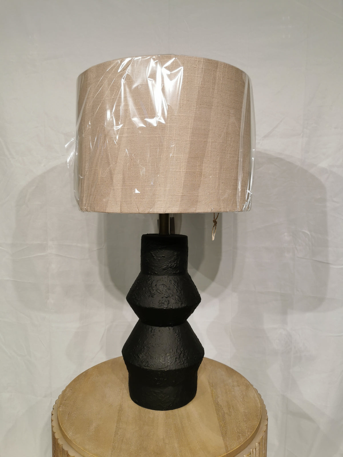 The Noelle Table Lamp by Adesso Lamp features a beige fabric shade and black textured ceramic base on a wooden table.