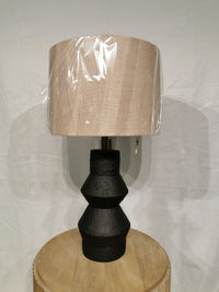 The Noelle Table Lamp by Adesso Lamp features a beige fabric shade and black textured ceramic base on a wooden table.
