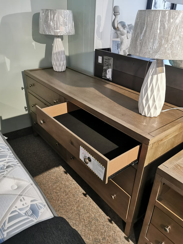 The Donald Choi Winston 6 Drawer Dresser in vintage walnut is displayed with two white lamps in the showroom.