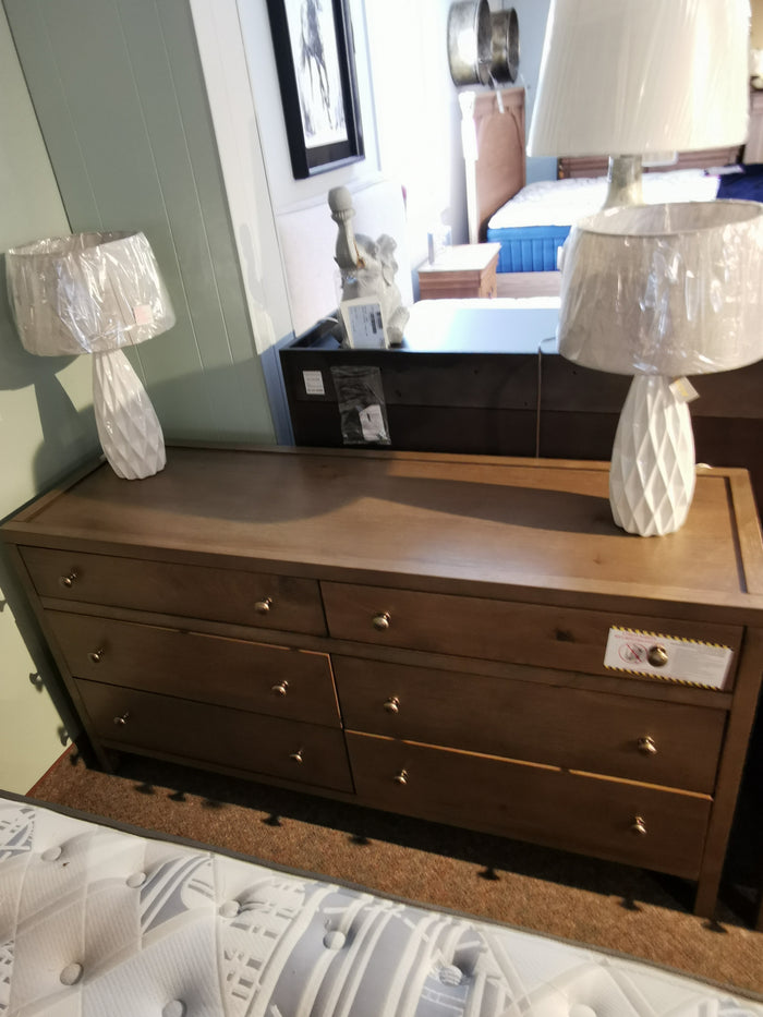 Donald Choi Winston 6 Drawer Dresser in vintage walnut, two white lamps, and a mirror displayed in a showroom.