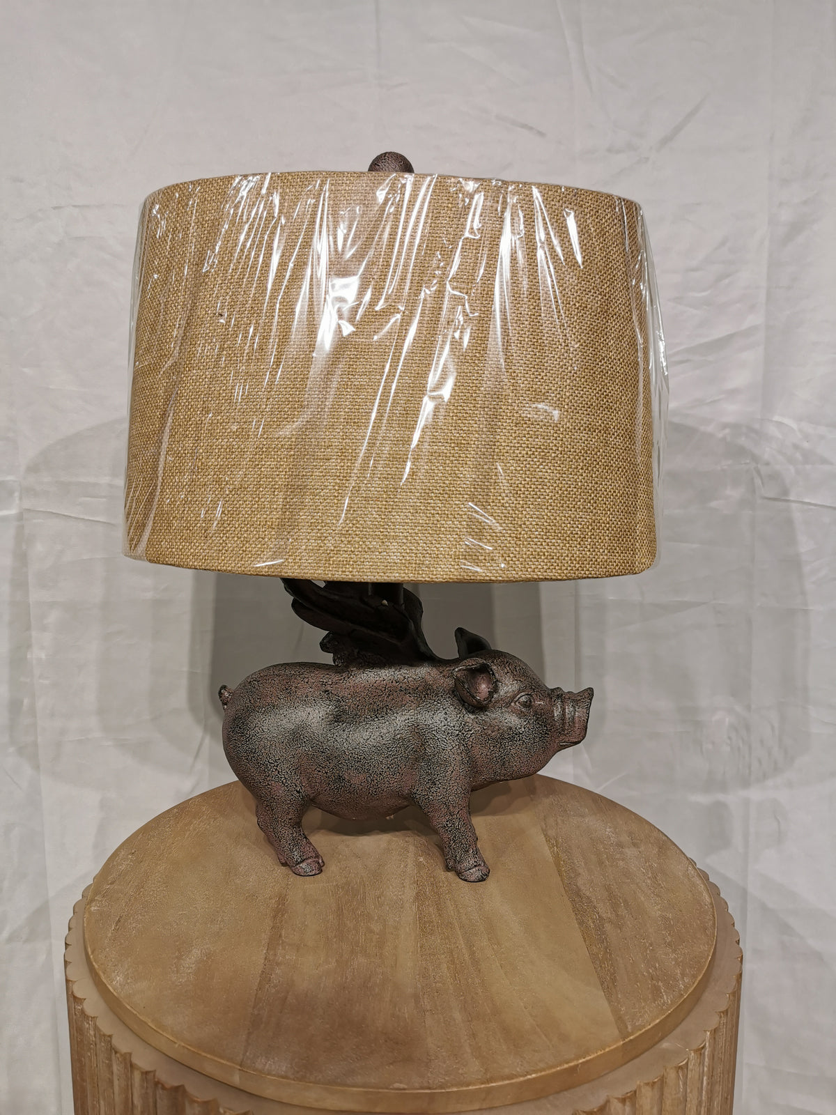 The Hogs Fly Table Lamp by Crestview Collection has a pig base and beige shade on a rustic wooden table.