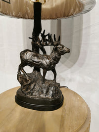 Hunters Walk Table Lamp by Crestview Collection features a bronze deer statue base on a rustic table with a white background.