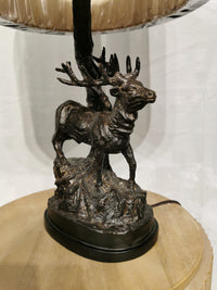 The Crestview Collection Hunters Walk Table Lamp has a bronze deer sculpture base on a rustic wooden table.