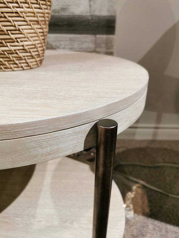 Close-up of the Magnussen T5927 Jennings Round End Table, Edgecomb Grey, with black metal legs and a woven basket on top.