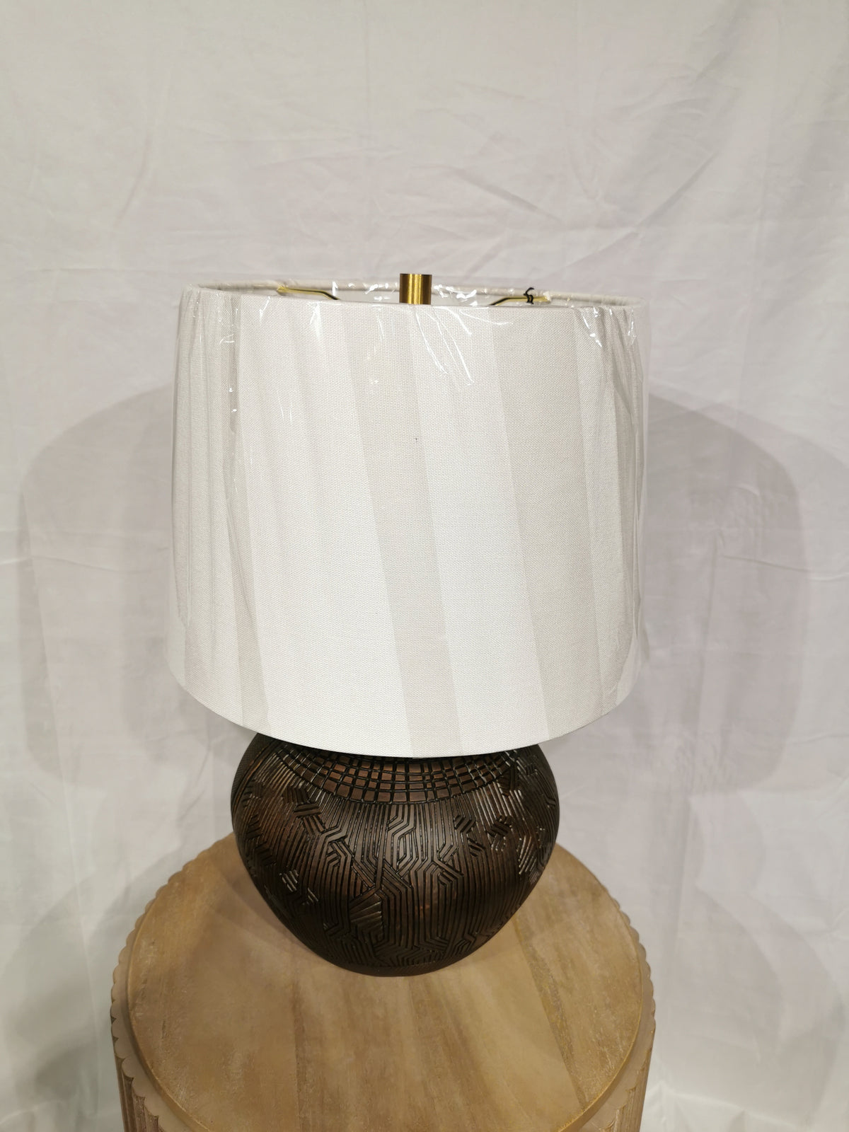 A Crestview Collection Reine Table Lamp with a round pattern and white shade sits on a wooden table against a plain backdrop.