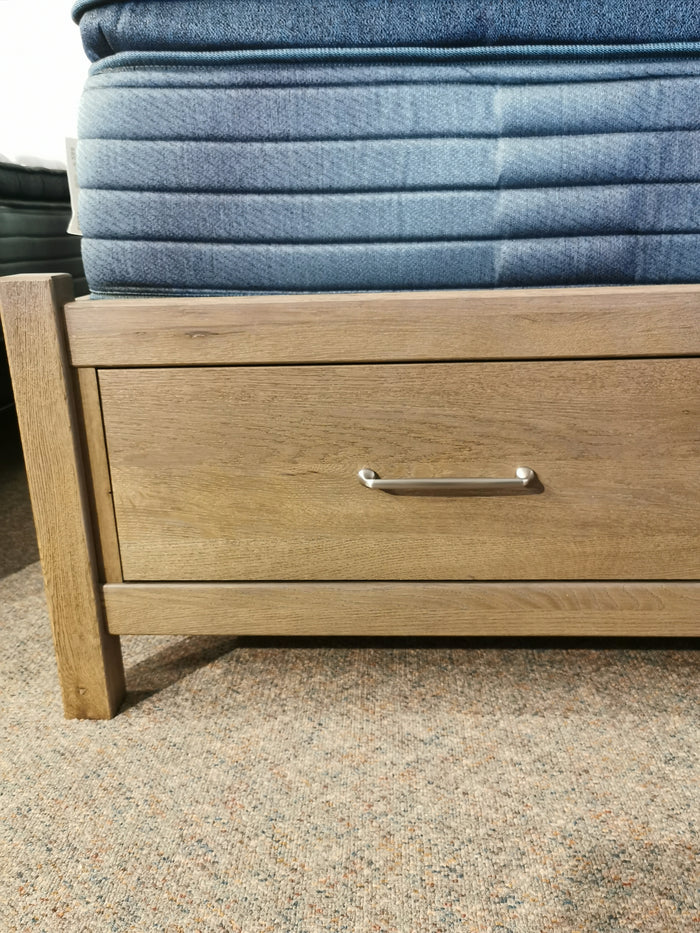Vaughan Bassett 831 Pencil Post Tide & Timber Queen Bed on carpeted floor with built-in drawer and silver handle.