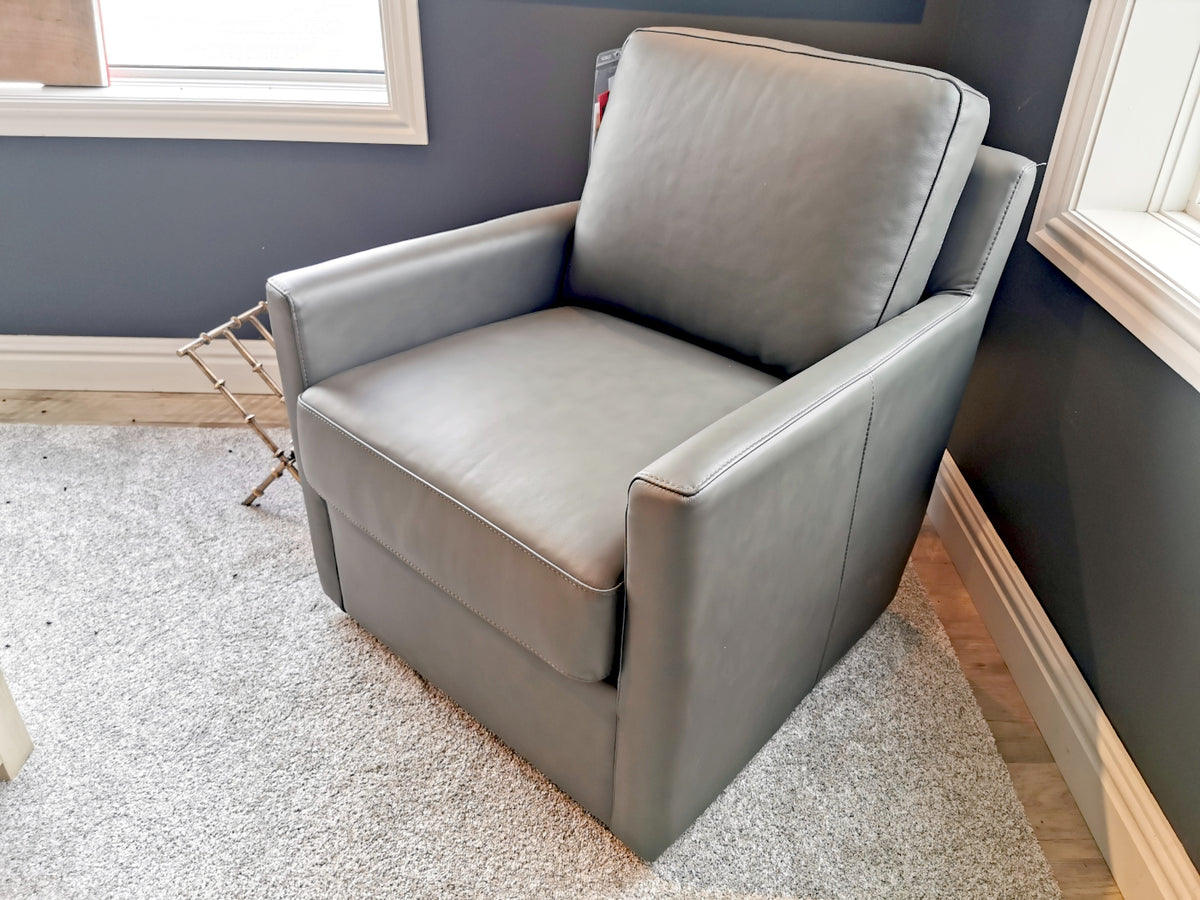 The 733 Leather Swivel Chair by Leather Craft, in gray leather, sits on a light carpet by two corner windows.