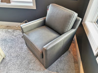 The 733 Leather Swivel Chair by Leather Craft, upholstered in gray leather, sits by a window and dark wall on carpet.