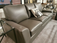 The Kent Sofa (Armani Grey) by Leather Craft exudes style, paired with a pillow and framed by glass tables and neutral decor.