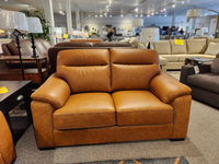 The Norway Leather Loveseat by Leather Craft is on display, surrounded by top-grain leather furniture and tagged lamps.