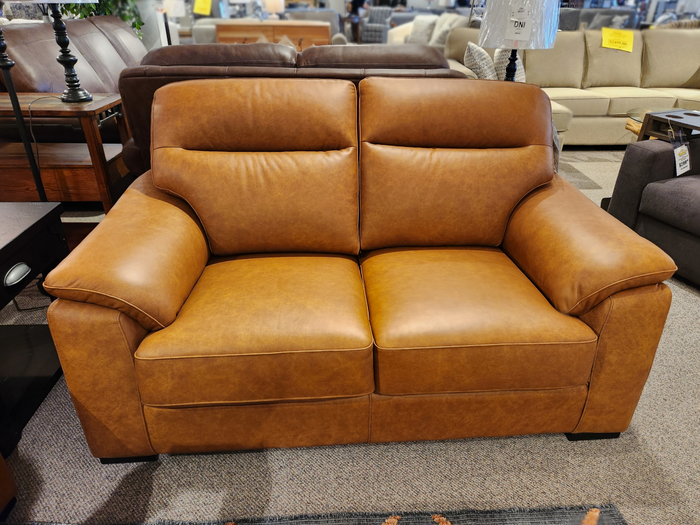 The Leather Craft Norway Leather Loveseat with wide armrests and cushioned seats is displayed in the showroom.
