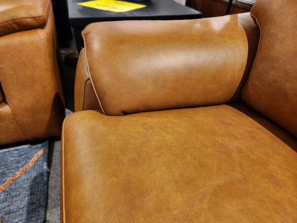 Close-up of Norway Leather Loveseat by Leather Craft, showing tan top-grain leather arm and seat cushion, table and rug behind.