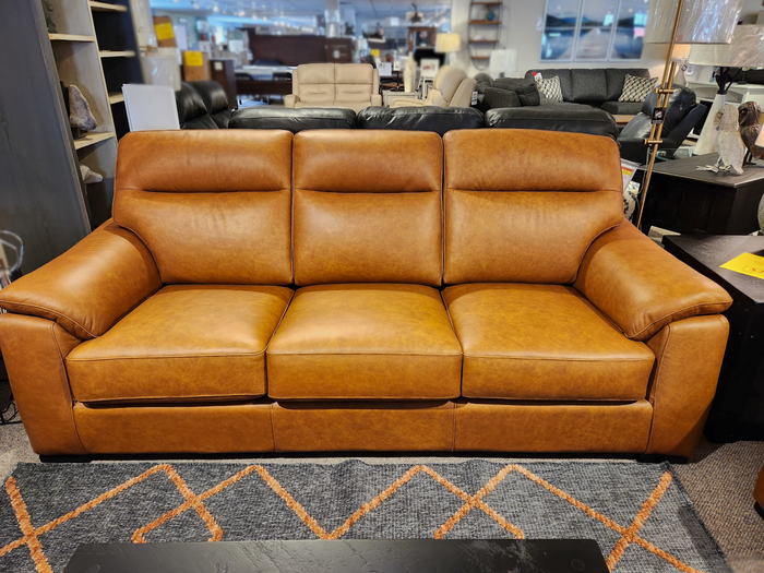 The Leather Craft Norway Leather Sofa is displayed in a showroom on a rug with an orange diamond pattern.