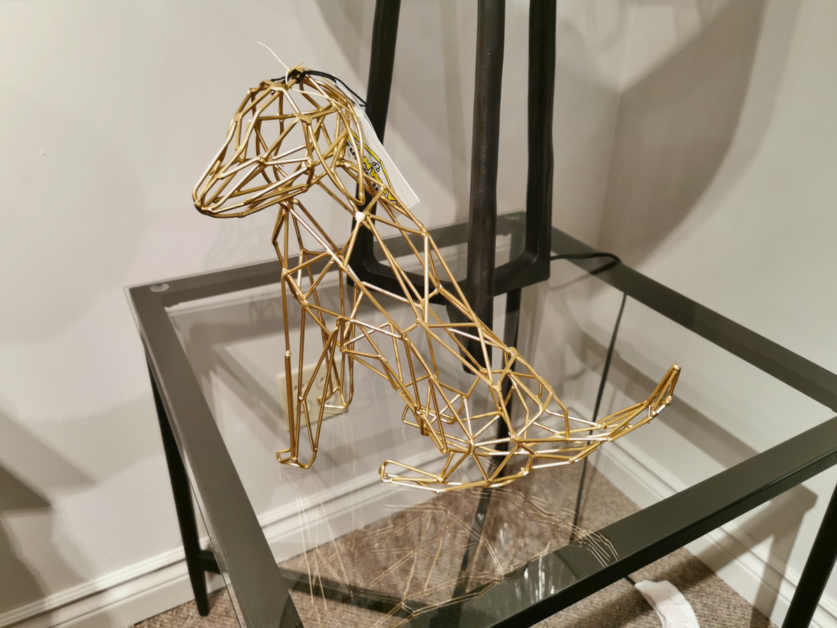 The Mercana 67883 Frankie I matte gold dog decor sits on a glass table in a modern, minimal room.