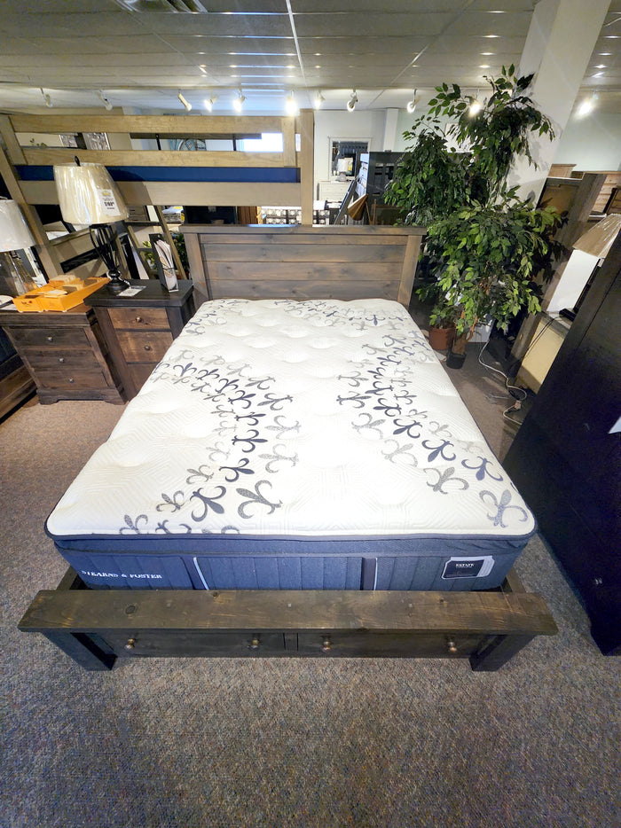 Mon Amour Euro-Top Plush Mattress by Stearns & Foster on a wooden bed in a store display, surrounded by furniture and a plant.