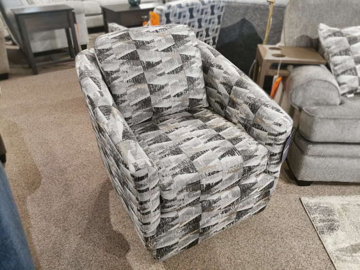 In a Toronto furniture showroom, the 312 Swivel Chair by Superstyle features a compact design with patterned gray and white upholstery and an elegant button-back detail, elegantly resting on a carpeted floor.