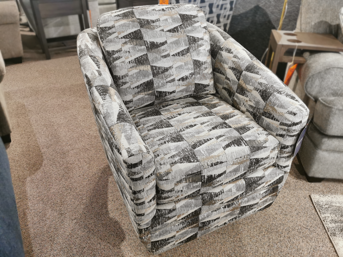 The 312 Swivel Chair from Superstyle, featuring a patterned gray design and a button back, sits elegantly on the carpeted floor of a Toronto furniture store display.