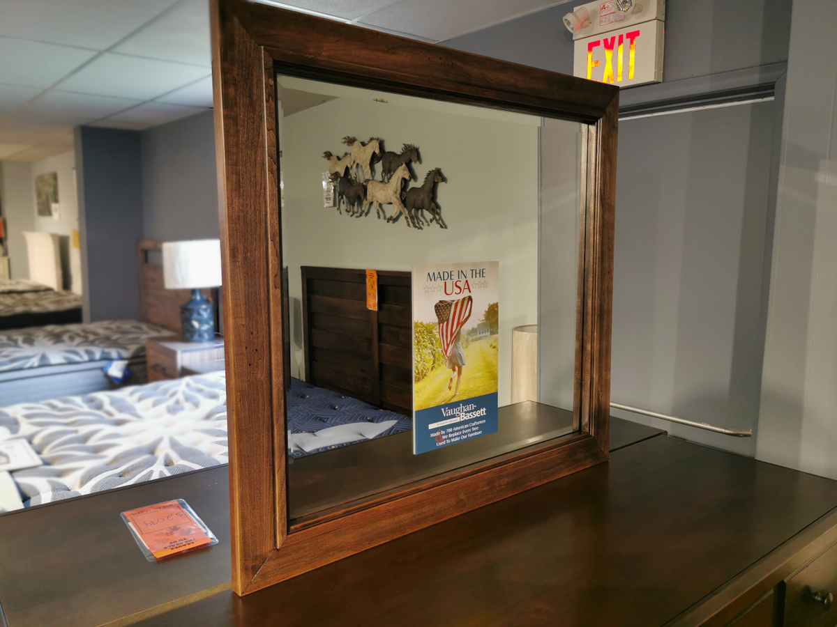 The Vaughan Bassett Landscape Lancaster Mirror on a dresser reflects a bed, wall art, and mattress sign.