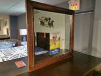 The Vaughan Bassett Landscape Lancaster Mirror on a dresser reflects a bed, wall art, and mattress sign.