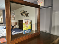 The Landscape Lancaster Mirror by Vaughan Bassett reflects a bed and a "Made in the USA" mattress brand sign.