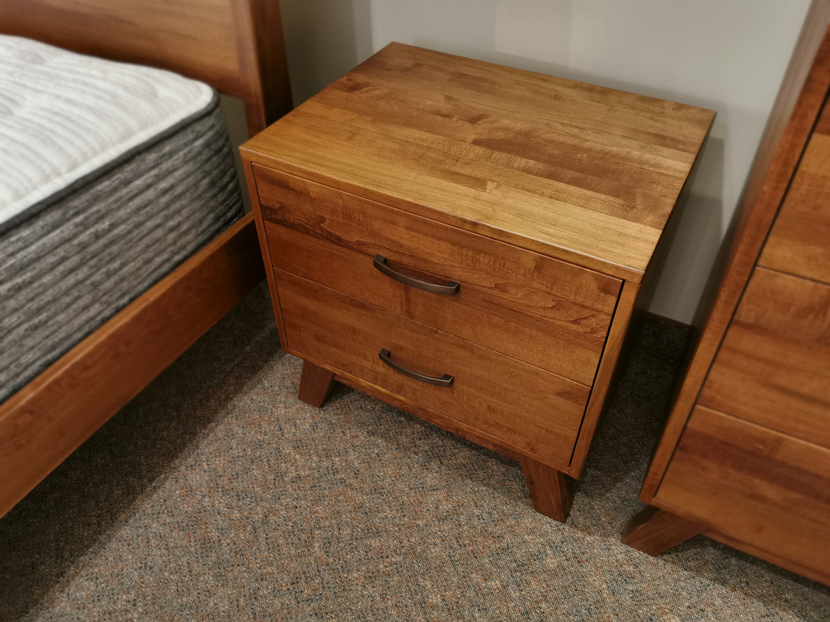 The Vokes Rocklynd 2 Drawer Night Stand, modern with dark handles, sits on a carpeted floor.