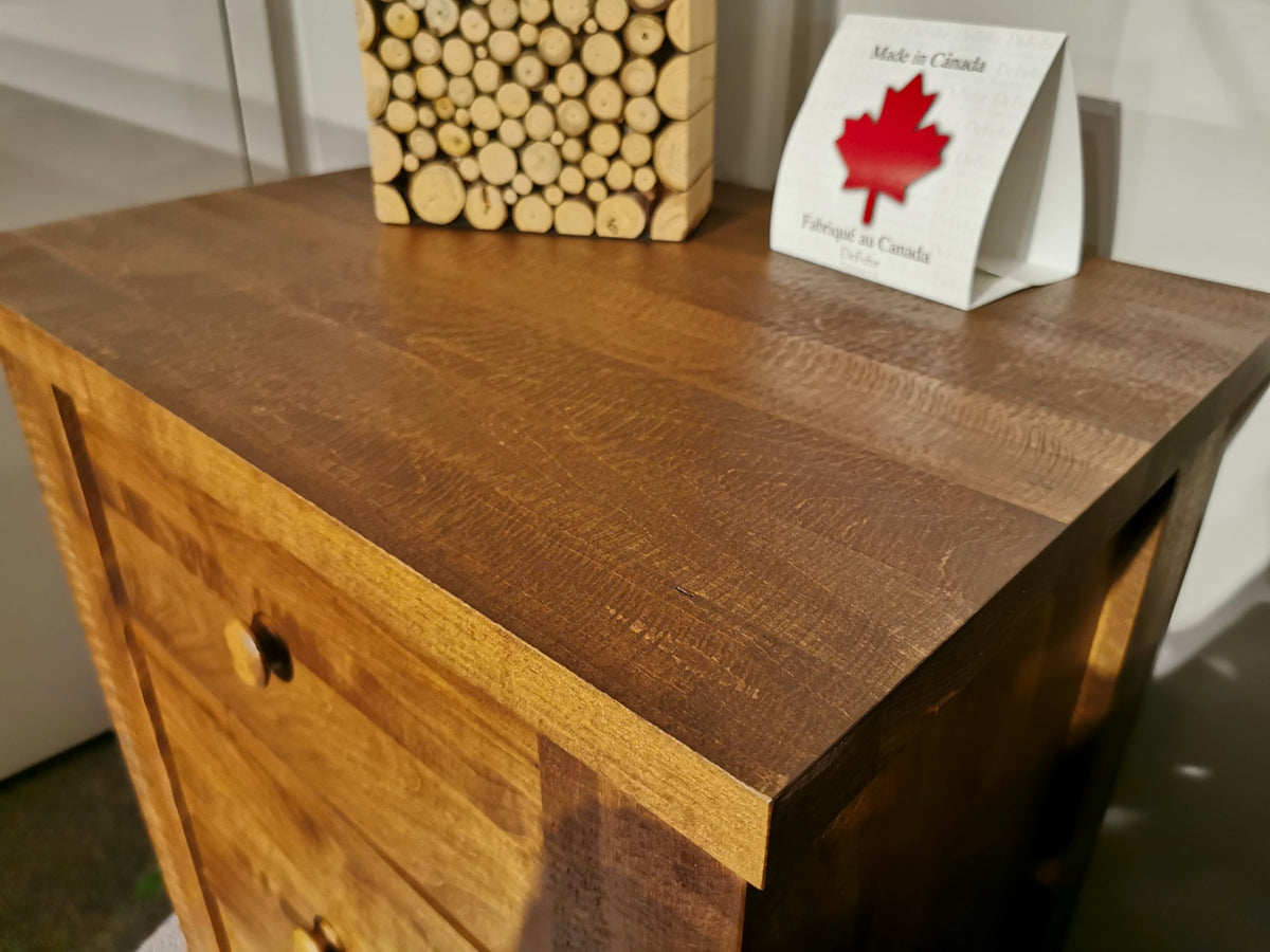 The 250 Roughsawn 3-Drawer Night Table by Vokes features a rustic wooden design with three drawers, a decorative block of wood circles, and a "Made in Canada" emblem with a red maple leaf. Crafted from warmy maple, it showcases provincial finishes that enhance its timeless appeal.