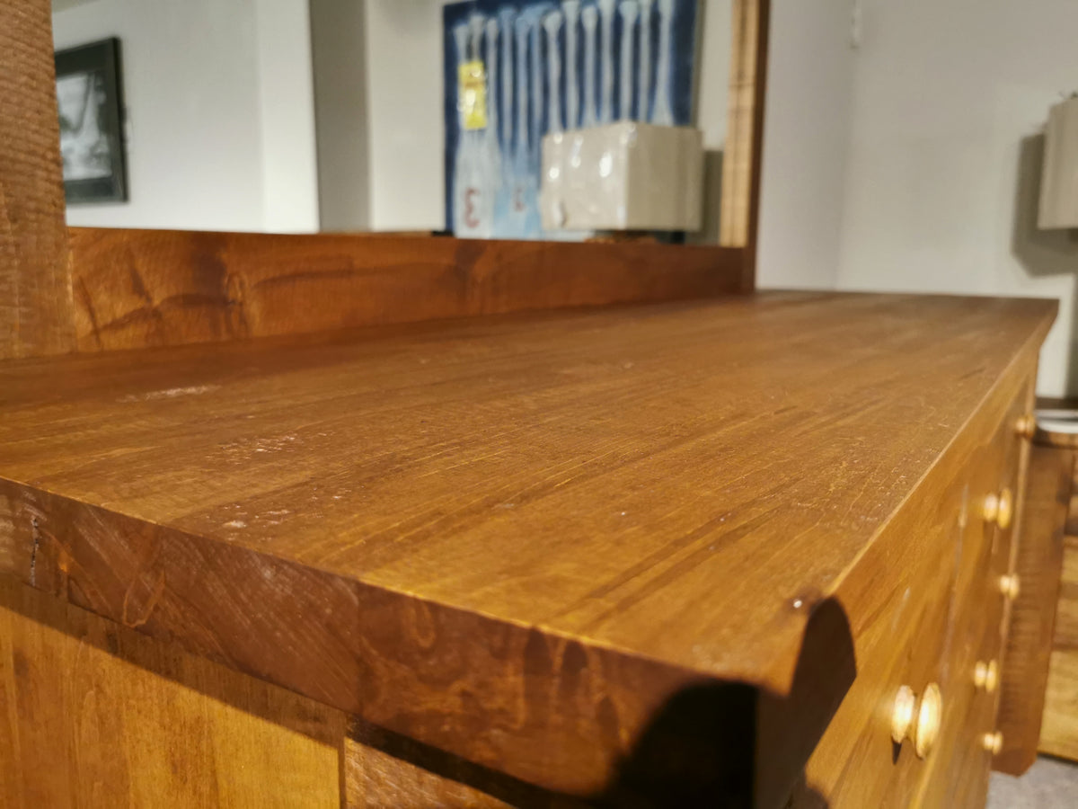 Close-up of the Vokes 250 Rough Sawn 9-Drawer Dresser, featuring round knobs and a smooth surface against framed art.