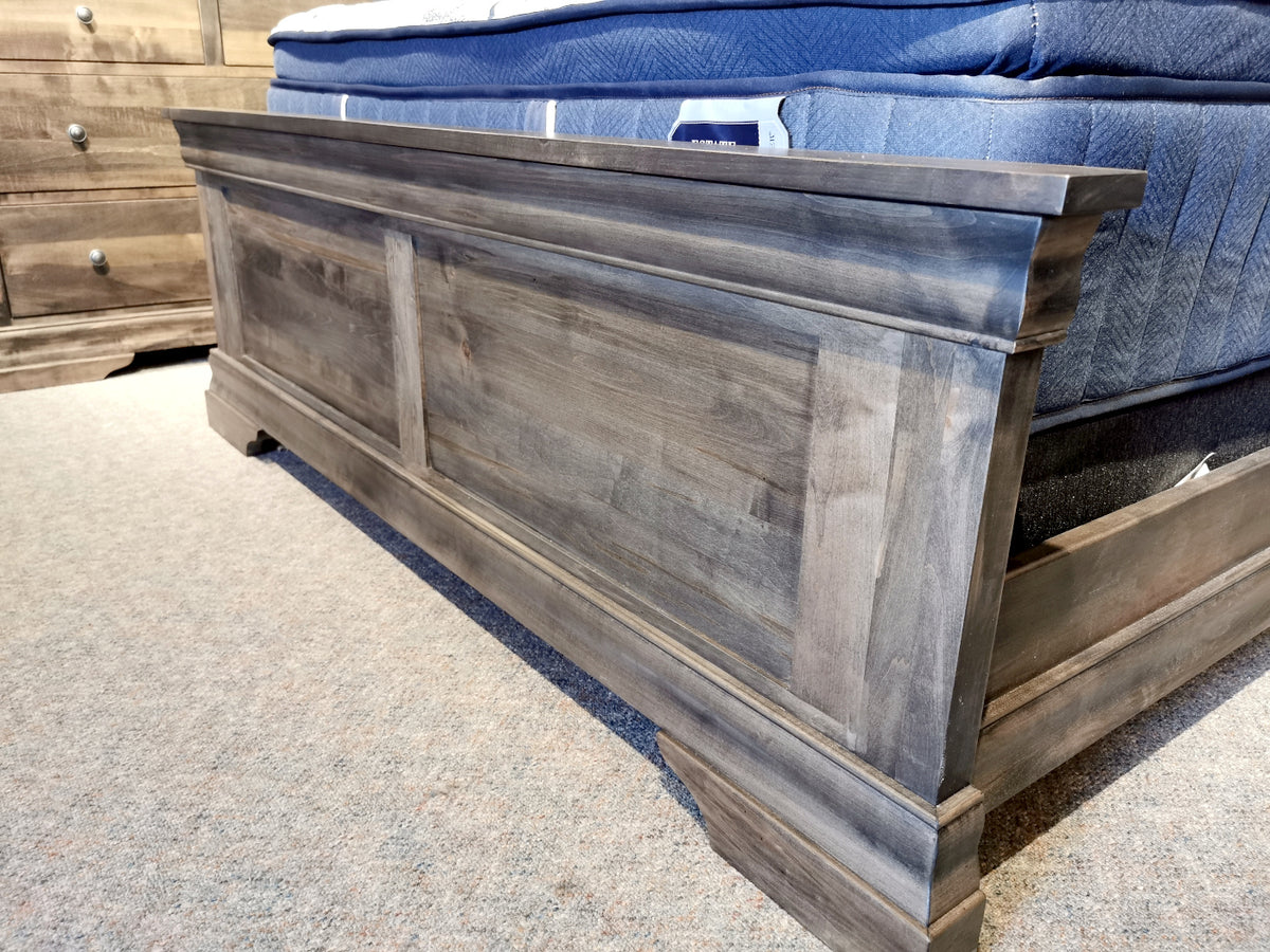 A Vokes 262 Bayshore Queen Panel Bed with decorative moulding and blue mattress sits on a carpeted floor.