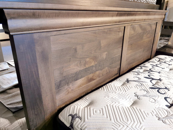 Close-up of a Vokes 262 Bayshore Queen Panel Bed with panel headboard next to a white patterned mattress in a showroom.