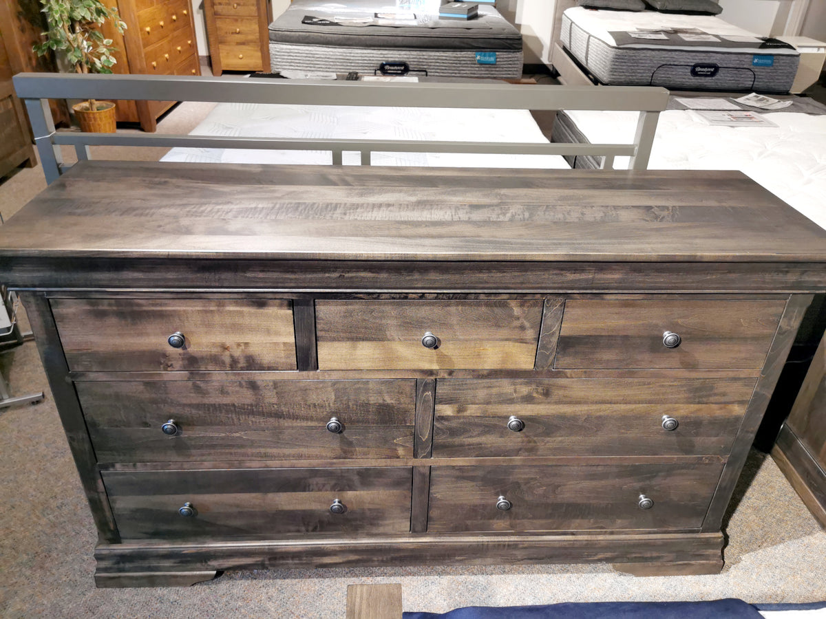 The Vokes 462 Bayshore 7-Drawer Dresser with metal knobs is shown in a showroom, mattresses in the background.
