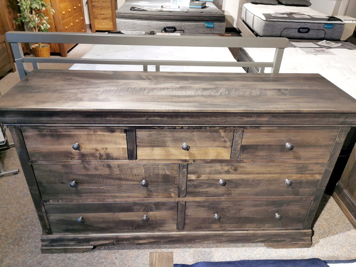 The Vokes 462 Bayshore 7-Drawer Dresser with metal knobs is shown in a showroom, mattresses in the background.