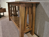 The NP100S Newport Sofa Table, by Winners Only, features a slatted shelf and sits against a gray couch on carpet.